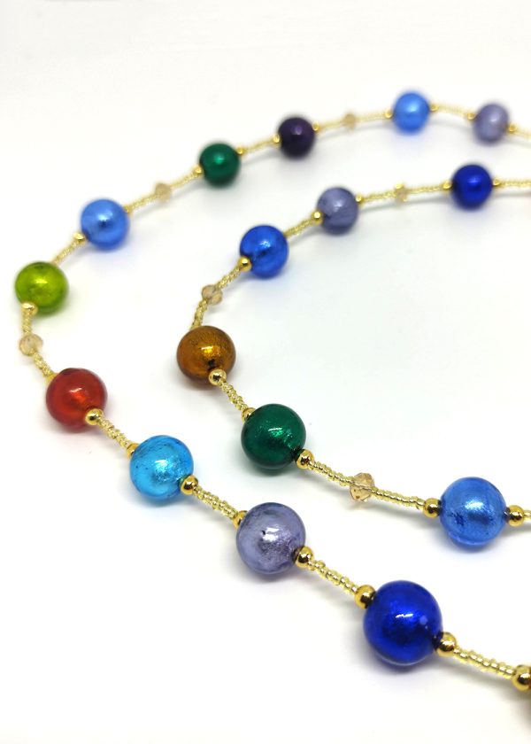 Image with partial detail of a necklace with colored glass beads in cobalt blue, sky blue, baby blue, gold, red, green and lavender separated by tiny gold glass beads and golden crystals
