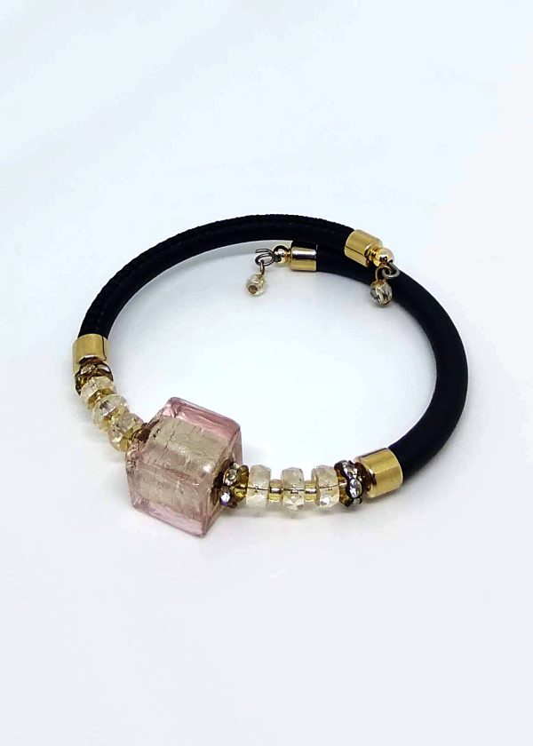 The bracelet features a pink glass centerpiece that encapsulates a delicate golden bead. On either side, a sequence of gold and clear beads is meticulously arranged in an alternating pattern. Completing the ensemble is a refined black band.
