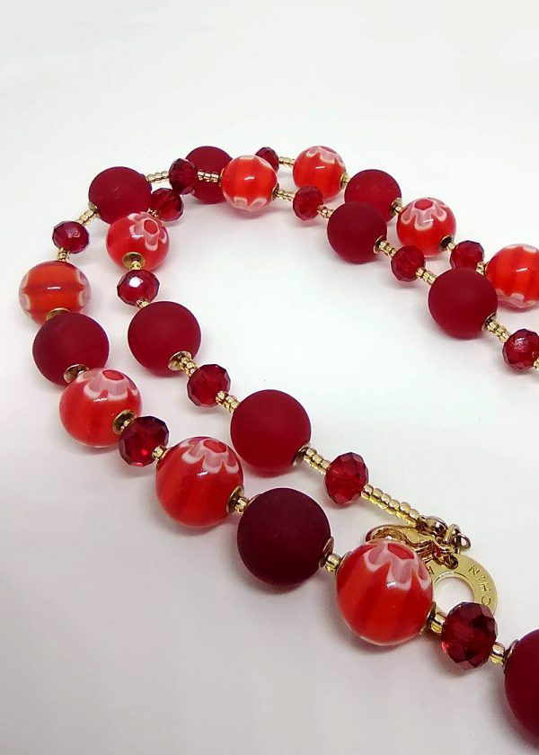 Detail of a necklace with blood red frosted beads, red crystal and delicate red and orange striped beads, each with a millefiore flowers separated by tiny golden glass beads.