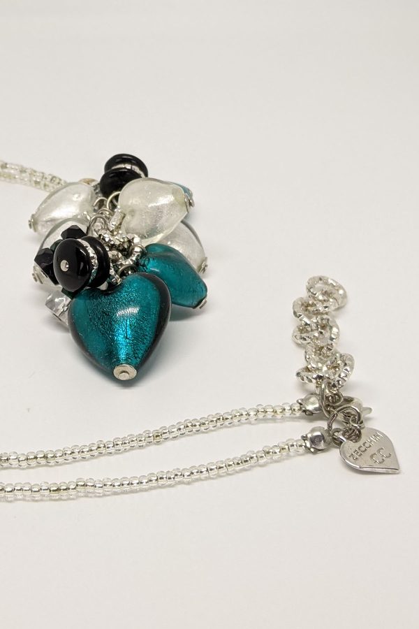 White and peacock-colored hearts are combined with green, silver, black, and transparent beads to create a unique focal point in this gorgeous necklace. The pendant and delicate beading throughout add to its charm.