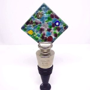 Wine stopper with a square base made of bright greens, blues, and purples, with a splash of mismatched flowers.